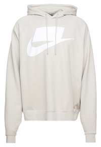 Ljus beige hoodie med en stor vit Nike-logotyp, dragsnören vid huvan och ribbad mudd och nederkant. Mjukt, texturerat tyg.