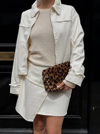 Valge denimpusa kärbitud servadega, beežist kudumist topp ja kreemivärvi seelik; hoiab käes pruunikat leopardimustriga käekotti. Rühmitatud värvid loovad kontrasti.