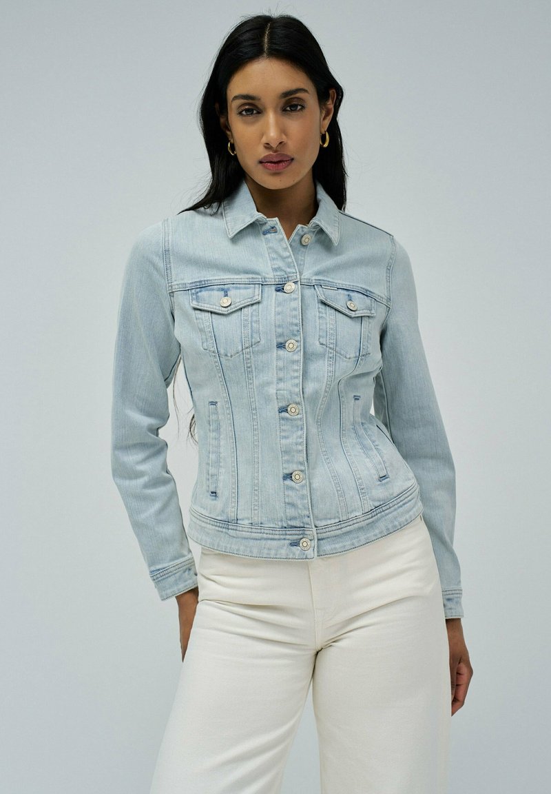 Veste en denim bleu clair à manches longues, avec des boutons et deux poches poitrine. Texture lisse avec une coupe légèrement ajustée.