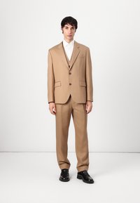 Beige tailored suit with a single-breasted jacket, notch lapels, two front pockets, and matching trousers. Worn with a white shirt and black shoes.