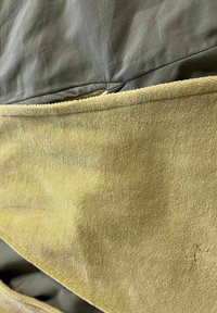 Vihreä kangas päällä, jossa on sileä pinta, kerrostettuna alla olevan keltaisen, pörröisen materiaalin päälle. Reunakaitaleet ovat näkyvissä, mikä osoittaa rakenteellisia yksityiskohtia.