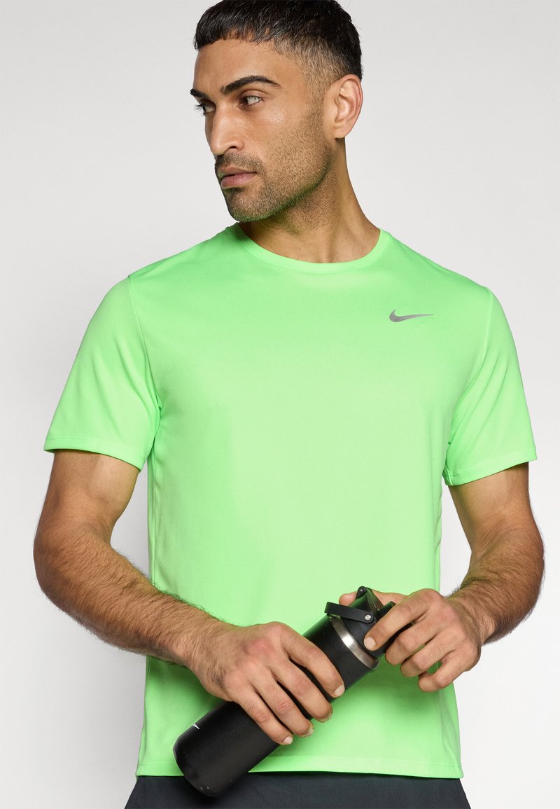 Limettengrünes Sport-T-Shirt mit Rundhalsausschnitt, kurzen Ärmeln und einem dezenten silbernen Nike-Logo. Das Modell hält eine schwarze Wasserflasche.