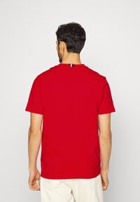 T-shirt in cotone rosso con maniche corte, scollatura rotonda e cuciture a forma di V sul retro. Presenta un piccolo etichetta colorata.
