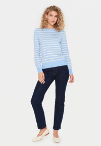 Pull rayé bleu clair avec des lignes horizontales crème, poignets et ourlet côtelés, associé à un jean bleu foncé et des ballerines crème. Tenue décontractée présentée.