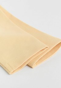 Acercamiento de los extremos de mangas de tela beige con dobladillos de doble costura sobre un fondo claro.