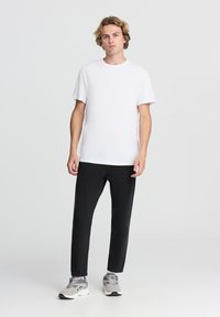 T-shirt bianco a maniche corte abbinato a pantaloni neri skinny. Il modello indossa sneakers grigie e bianche con un design texturizzato.