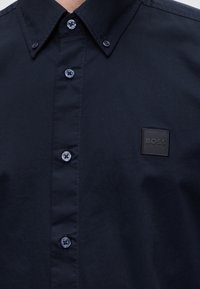 Chemise bleu marine foncé à boutons avec un col pointu et un patch carré avec le mot BOSS sur la poitrine gauche.