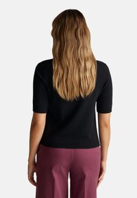 Černý krátký rukáv pletený top s přiléhavým střihem, hladkou texturou a žebrovanými manžetami, zkombinovaný s růžovými širokými kalhotami.