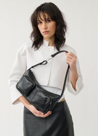 Sac en cuir noir à bandoulière avec deux poches zippées à l'avant, texture lisse, sangle réglable et détails de couture subtils.