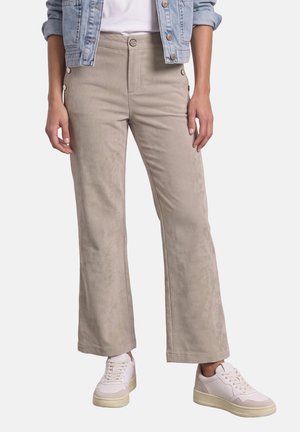 Personne portant un pantalon large en velours côtelé beige, des baskets blanches, une chemise blanche et une veste en jean bleu clair avec les manches retroussées.