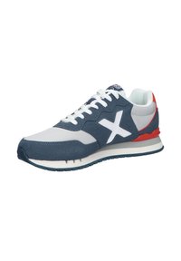 Zapatilla deportiva de color azul marino y gris con detalles en blanco, tela texturizada, suela acolchada y un detalle en rojo en el talón. Presenta un diseño con cordones.