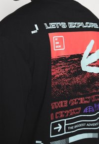 Svart t-shirt med vibrerande grafik, inklusive text och handdesigns i rött, vitt och blått. Anmärkningsvärda tryckta accenter förstärker dess visuella tilltalande.