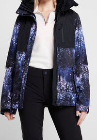 Wasserabweisende Jacke in Schwarz und Blau mit einem Galaxiemuster. Verfügt über eine Kapuze, mehrere Reißverschlusstaschen und ein weiches Innenfutter.