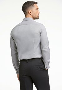Graues, knopfdown Hemd mit einem subtilen geometrischen Muster, langen Ärmeln und Manschettendetails, kombiniert mit dunklen, maßgeschneiderten Hosen.