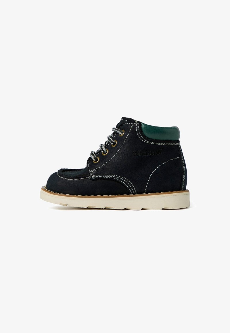 Bottines noires en suède à lacets avec un col vert, des coutures blanches et une semelle en caoutchouc beige. Présente des œillets en métal ronds et une texture lisse.