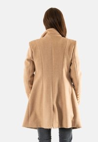 Cappotto beige a spina di pesce con colletto alto, silhouette svasata e bottoni oversize sulle maniche. Materiale in morbida miscela di lana.