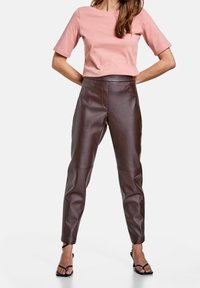 Ljusrosa t-shirt med kort ärm, som parats med högmidjade bruna läderbyxor. Byxorna har en slät textur med en åtsittande design och smala ben.