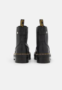 Black leather ankle boots with a matte finish, yellow stitching, pull tab, and chunky rubber sole. Features a strap and snap button detail.