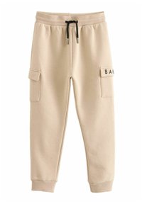 Pantalones de chándal beige hechos de una tela suave, con bolsillos laterales, una cintura con cordón y un parche con 'BAK' en el muslo derecho.