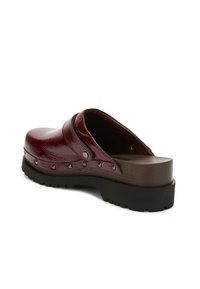 Zueco de charol burdeos con un acabado suave, acentos negros, punta redondeada y tachuelas metálicas decorativas a lo largo del lateral. Suela de goma gruesa.