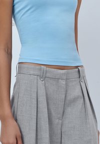 Light blue fitted tank top paired with gray pleated trousers. Trousers have a textured fabric with belt loops and a tailored waistband.