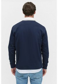 Marinblus med lång ärm och vit krage, tyget har en slät struktur, rak fåll och minimal detaljering på baksidan.