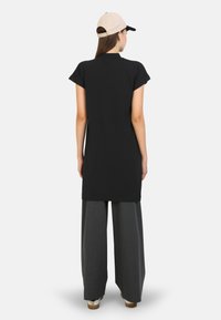 Tunic nera con maniche corte, abbinata a pantaloni grigi larghi. Modella con un berretto beige, che mostra una silhouette semplice e rilassata.