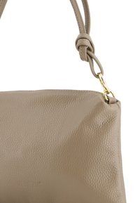 Beige læder håndtaske med struktureret overflade, en knyttet rem og hardware i guldtoner til fastgørelse. Lynlåslukning i toppen.