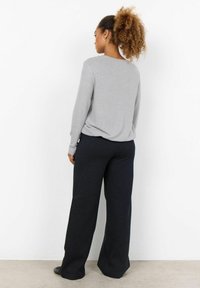 Grijze lange mouw top met een ronde hals, gecombineerd met zwarte geruite wijde broek. De outfit heeft een relaxte pasvorm en een zachte textuur.