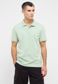 Šviesiai žalias medvilninis polo marškinėlis su trimis sagutėmis, trumpomis rankovėmis ir mažu logotipu ant krūtinės. Juodos cargo šortai.