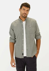 Zwart-wit geblokt overhemd met opgerolde mouwen, gedragen over een wit t-shirt. Het overhemd heeft een zak aan de linkerkant.