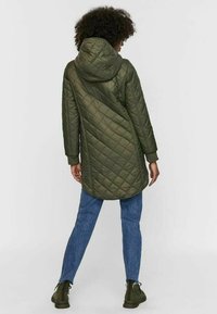 Olivgrön kviltad lång jacka med huva, med ett texturerat mönster, avslappnad passform och ribbade manschetter, i kombination med blå jeans och stövlar.