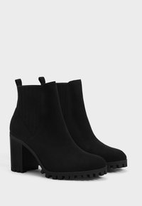 Black ankle boots made of suede, featuring a rounded toe, ribbed side panels, and a chunky, textured heel with a lug sole.
