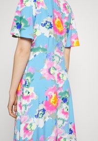 Vestido floral em tecido leve com um fundo azul e padrões vibrantes de flores em rosa, amarelo e verde, com mangas curtas.