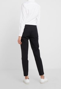 Czarne, dopasowane spodnie uszyte z lekkiego materiału, o wąskim kroju, z dwoma tylnymi kieszeniami na guziki, zestawione z białą koszulą z kołnierzykiem.