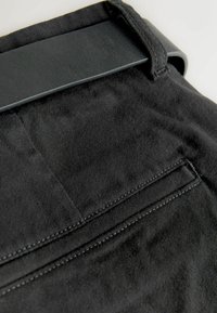 Fekete szövet nadrág sima textúrával, derékpánttal és egy hátsó zsebbel, egyenes varrással.