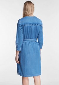 Denimmekko, jossa on vyöllinen vyötärö, aaltoileva yläosa, kolmannen osan hihat ja polveen asti ulottuva helma keskisinisenä.