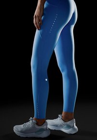 Zilas legingi ar gludu tekstūru, ar gradienta dizainu, smalkiem atreflectējošiem punktiem un logo. Kombinēti ar gaiši pelēkiem sporta apaviem.