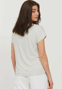 Top corto de manga corta en gris claro con cuello redondeado, textura suave y un ajuste relajado. Tejido liso con puños enrollados y sin patrones visibles.