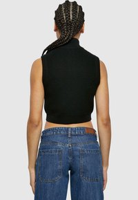 Svart stickad ärmlös topp med hög krage, tillsammans med medelhöga blå denimjeans med vanliga bakfickor och en läderlapp.