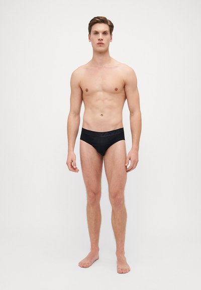 Costumi da bagno neri da uomo con finitura liscia, caratterizzati da un ampio elastico in vita e un design minimalista. Il tessuto appare elastico e confortevole.
