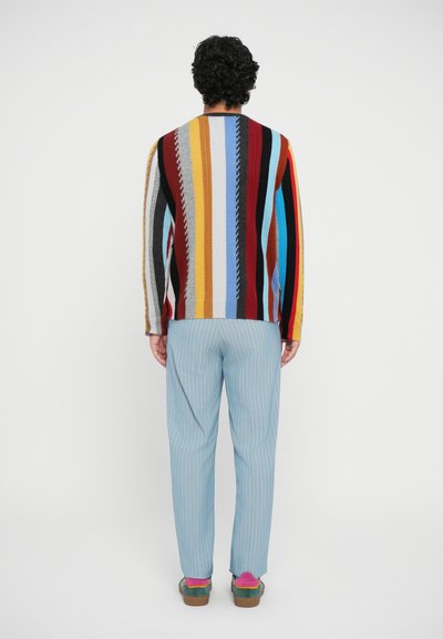 Multicolored knit sweater with vertical stripes, paired with light blue pinstriped trousers and colorful shoes with layered accents.