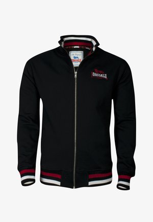 Svart zip-up jacka med ribbad krage och muddar. Har röda, vita och marinblå ränder på muddarna. Broderad logotyp på bröstet.