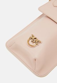 Różowa skórzana torba z akcentem w kolorze złotym w kształcie pierścienia, z dwoma wzorami ptaków, gładką fakturą i detalami przeszyć wzdłuż krawędzi.