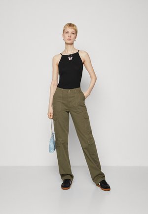 Top nero senza maniche con un dettaglio a forma di farfalla, abbinato a pantaloni cargo verdi oliva larghi con molte tasche e sneakers nere.