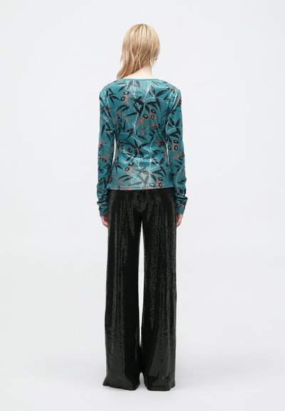 Haut à manches longues teal avec un motif botanique noir et orange, associé à un pantalon large à sequins noirs taille haute.