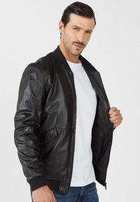 Zwarte leren bomberjack met een geribde kraag en manchetten, voorzien van een rits aan de voorkant en zijzakken. Soepele textuur met een getailleerd ontwerp.