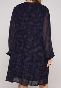 Mörk marinblå klänning med ett blommönster i blått, långa ärmar, lagerdesign och ett lätt, genomskinligt tyg.