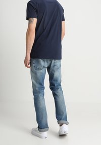 Mörkblå t-shirt med rund halsringning i kombination med ljusblå denimjeans. Jeansarna har en urtvättad finish, uppvikta ärmar och fickor med lappar. Vita sneakers fulländar looken.