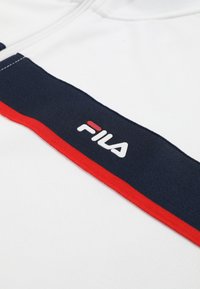 Hvidt stof med marineblåt og rødt vandret stribemønster med FILA-logo i hvide og røde bogstaver.